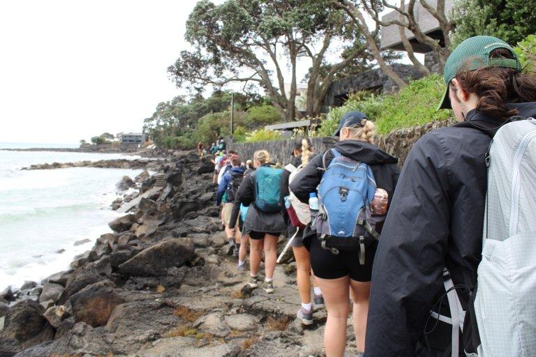 一排学生沿着黑色的岩石海岸线行走. 