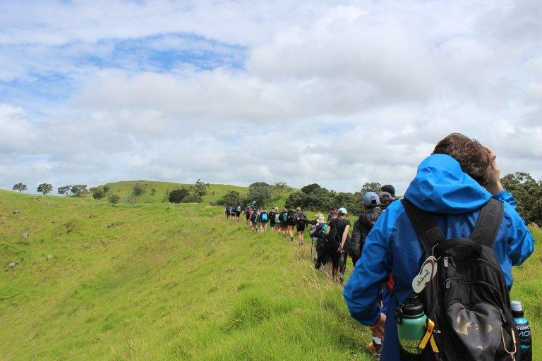 一排学生沿着长满绿草的山脊徒步旅行. 