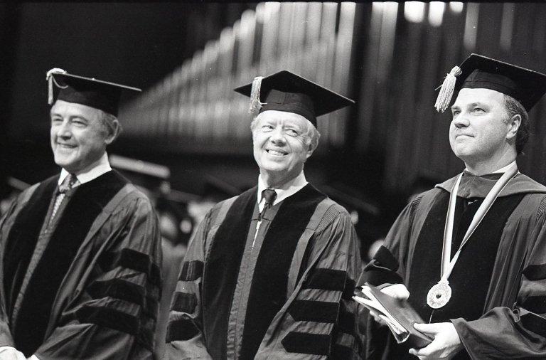 在毕业典礼上，前总统吉米·卡特身穿毕业袍，头戴毕业帽，站在其他人中间. 