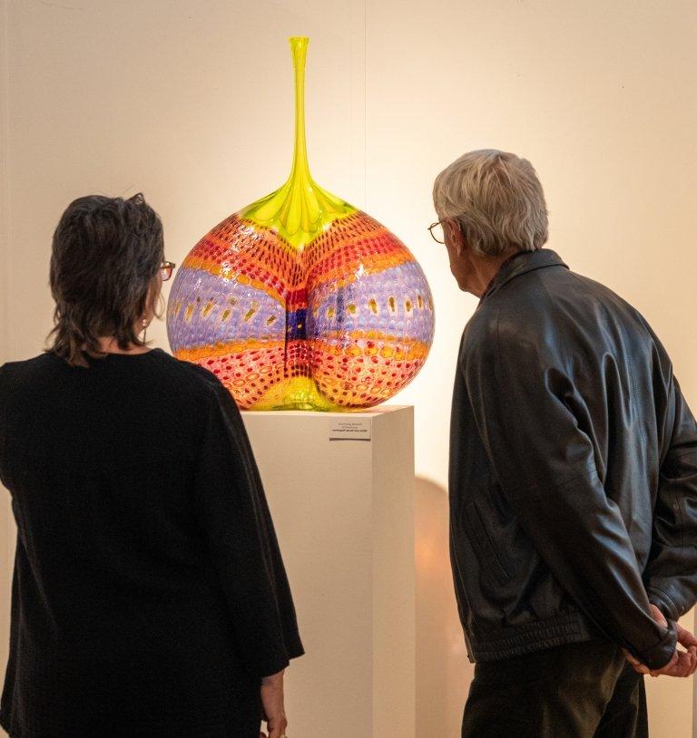 一个男人和一个女人仔细地看着博物馆里展出的色彩鲜艳的玻璃艺术容器. 