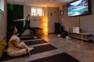 两名学生在配有大电视和瑜伽器材的房间里做瑜伽姿势. 