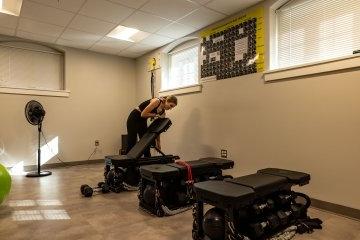一名学生在一个装有健身器材的小房间里调整三个锻炼长椅中的一个. 